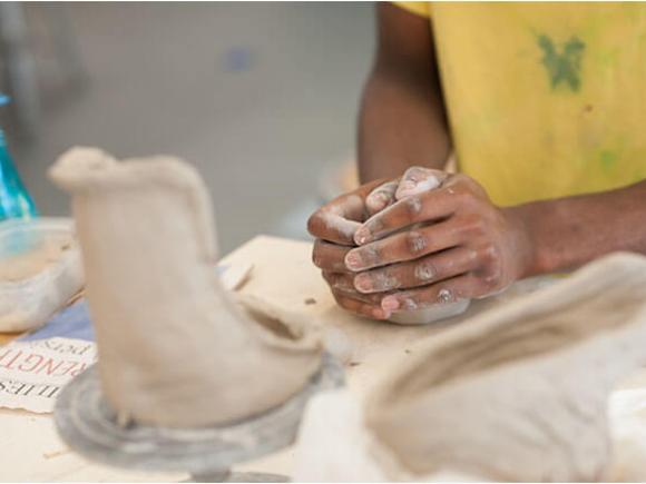 A student cups their hands next to several pieces of in-process ceramic artwork.
