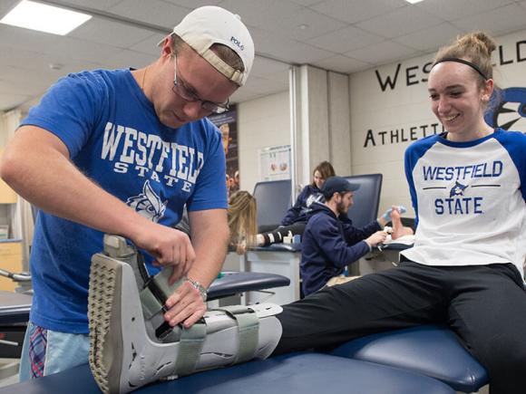 A Westfield State University student adjusts a walking boot cast worn by another student.