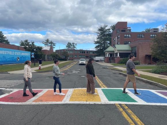 A rainbow sidewalk on campus, with four education majors mirroring the famous Beatles' album cover depicting the same.