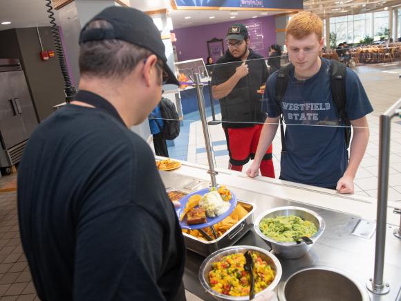 Student at Mexican food station wearing WSU navy shirt with staff member assisting him.