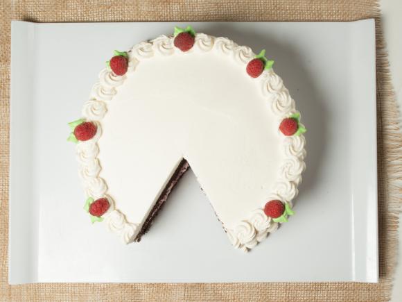 Chocolate cake with vanilla icing and raspberry accents on the top. Served on a white plate.