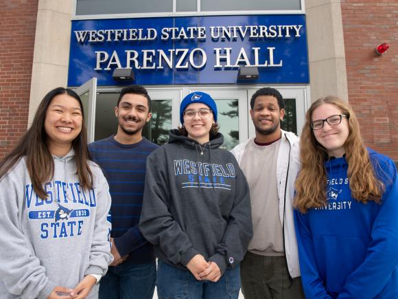 Five students wearing Westfield State sweatshirts smiling in front of Parenzo Hall.