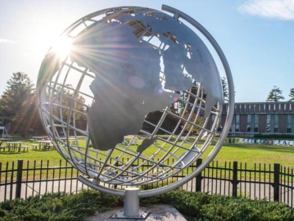 A metal globe sculpture sits in the middle of the Westfield State University campus green.