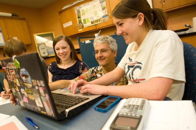 A faculty member assists two female students working on their laptop computer