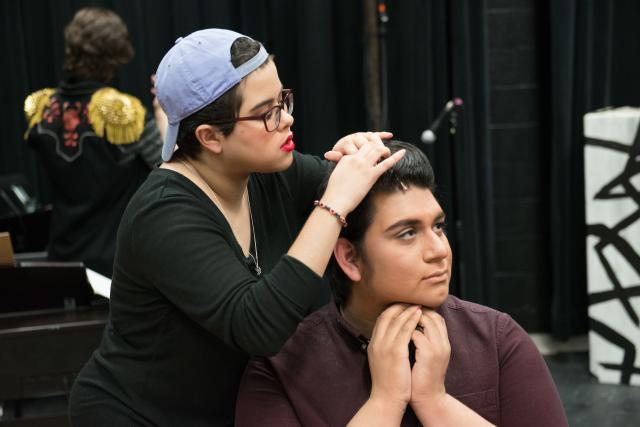 Stagehand setting up a wireless microphone on a student actor in the Ely Black Box theater prior to a performance