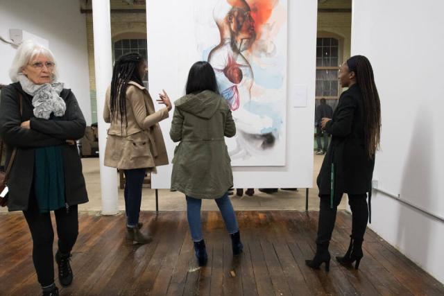Multiple people look a large painting displayed in a gallery setting.