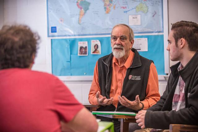 A professor talks with two students in a classroom setting.