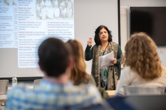 An ethnic and gender studies professor stands at the front of a classroom while teaching students.