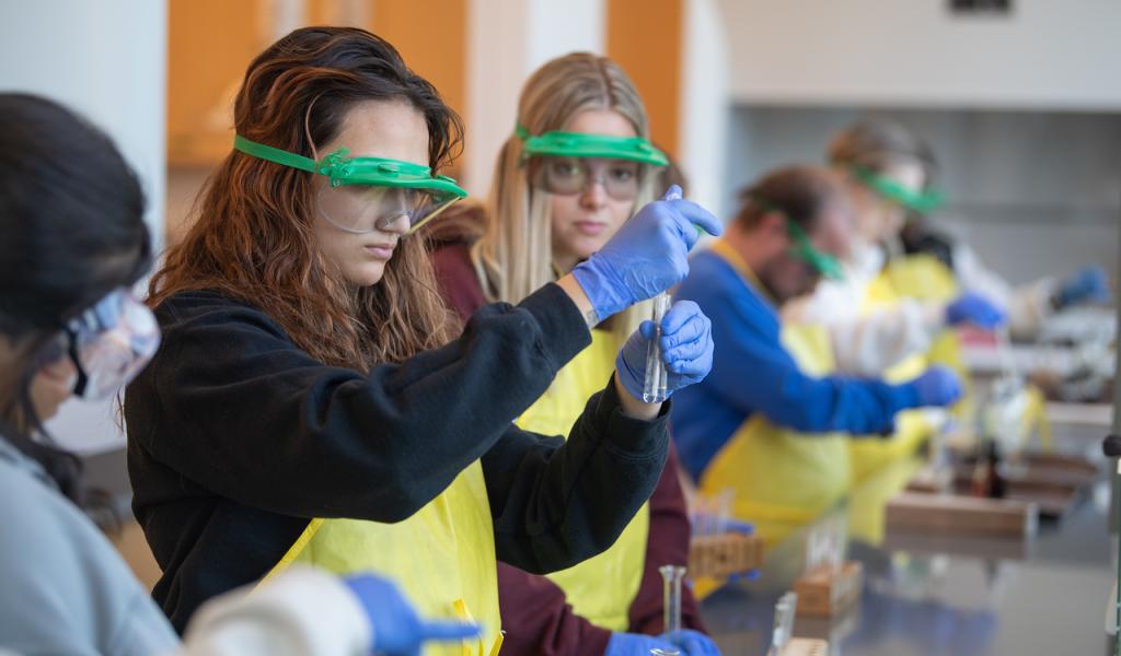 Chemistry students in a lab wearing eye protection and aprons.
