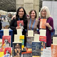 Carolina Hotchandani, a Latinx and South Asian poet, Rebecca Olander, Visiting Lecturer at Westfield State, Catherine Anderson, an older white-haired woman standing together at a booth full of poetry books. They are at the Association of Writers & Writing Programs conference.