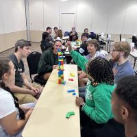 For RA Appreciation Week. Several students sit at a long, thin table, where they're playing jenga, a block-building game. They're being honored as part of RA Appreciation Week.