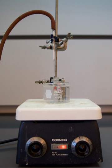 photo of a vial in a warm water bath with tubing and a pateur pipet position to blow compressed air over the surface of the evaporating solution