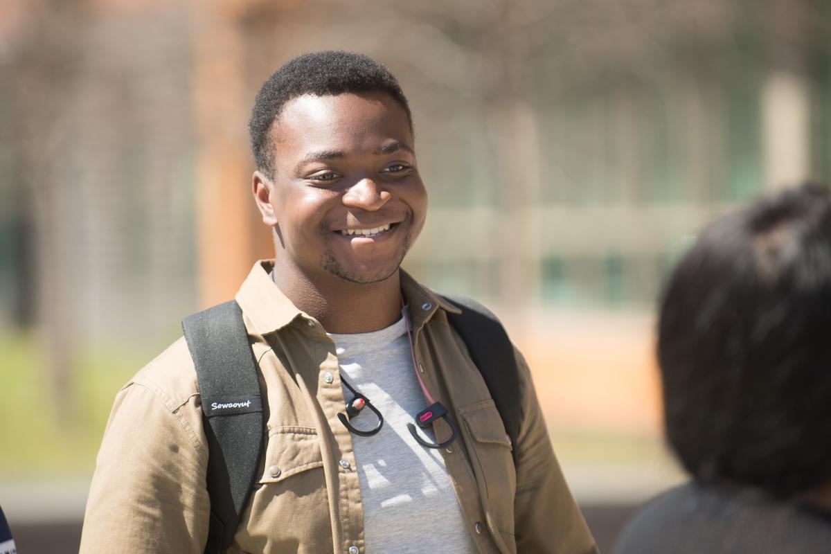 Smiling males student in light jacket with backpack on the campus green