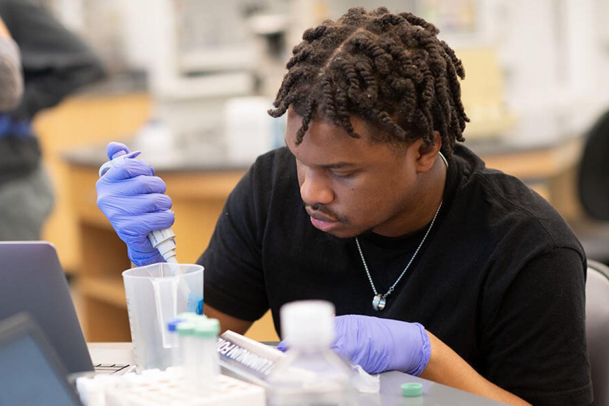 A student wearing rubber gloves conducts an experiment in a laboratory setting.