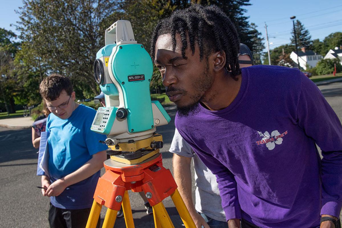 A student uses surveying equipment to take measurements.