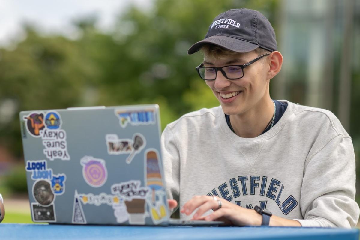Communication student smiling using a laptop.