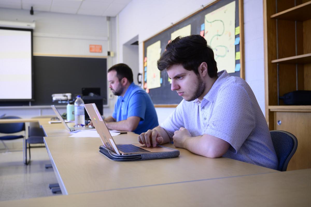 Two students part of the Western Mass Writing Project working on a desk with laptops.