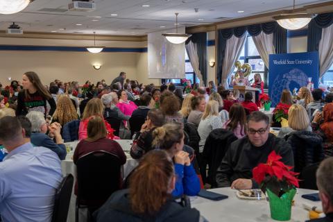 Large crowd of Westfield State employees sit at tables in Scanlon Banquet Hall decorated with poinsettias while President Linda Thompson reads names of raffle winners at the podium.