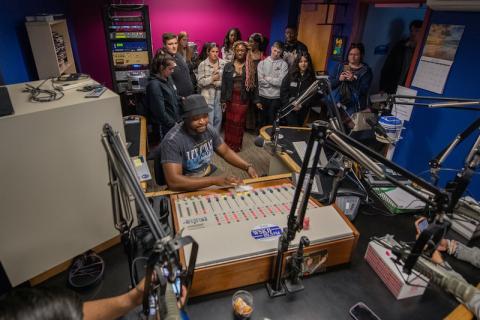 A group of students and an instructor gather around a recording studio.