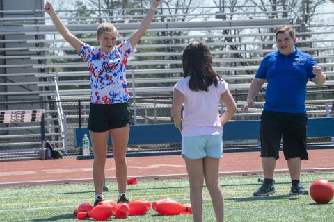 Two girls play sports, one older with her hands in the air celebrating while the younger girl smiles.