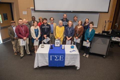 A group of students smiling and the symbol for Gamma Sigma Epsilon in front of them on a table.