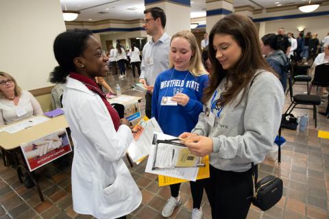 Three students are smiling and hold notebooks in their hand.