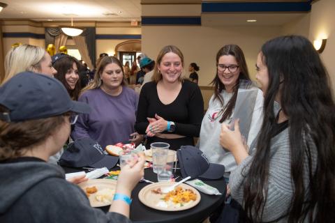 Students surround a table with food, smiling at each other.