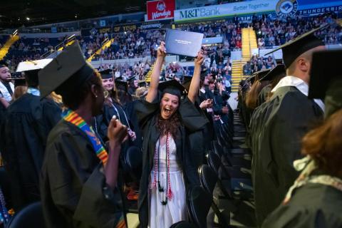 Students cheer and raise their diplomas at commencement.