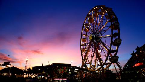 A photo of the sky, colored purple, pink, and yellow, with a silhouetted Ferris wheel in-frame.