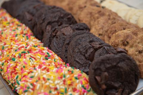 A close-up shot of three different kinds of cookies being offered in the Dining Commons. One is a white cookie with rainbow sprinkles, one is double-chocolate, and the third are brown cookies with chocolate chips.