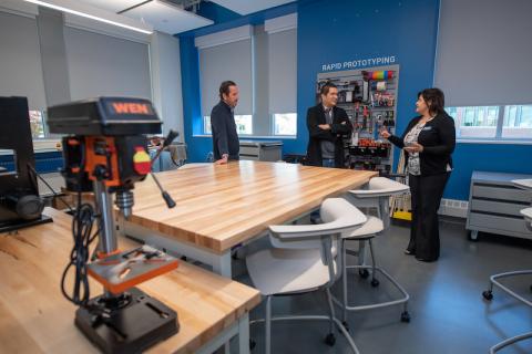 The new Research, Innovation, Design, and Entrepreneurial (RIDE) Center, with wooden tables, white chairs, blue walls, and three members of the Beveridge Foundation.