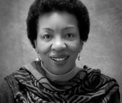 Dr. Shirley Whitaker. The photo is black and white and depicts a black woman smiling against a plain background. She wears a patterned scarf, dangly earrings, and is smiling at the camera.