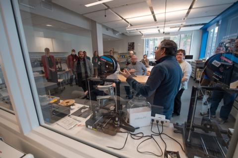 Faculty and staff gather at the RIDE Center as part of a two-day workshop on the new technology. They gather around a laser printer, 3D printer, and various other tools that will help enhance classroom work.