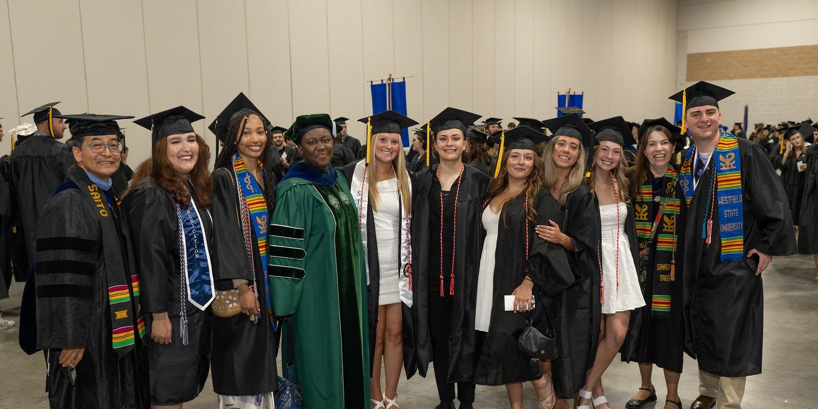 Students and faculty smiling in a group photo, wearing caps and gowns at commencement.