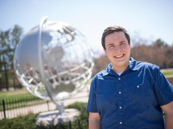 Photo of Aaron Lessing in front of the Globe sculpture one the campus green