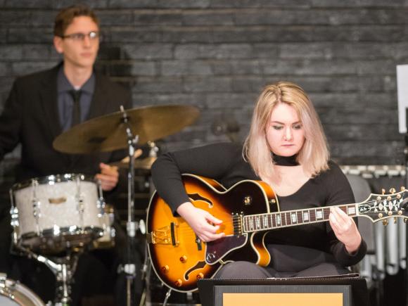 Female student playing guitar on stage as part of a jazz ensemble