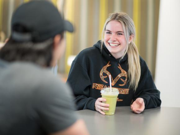 Smiling female talks to her friend while drinking a smoothie