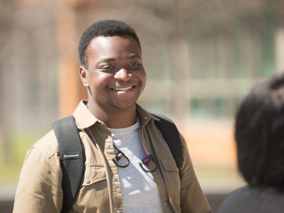 Smiling males student in light jacket with backpack on the campus green