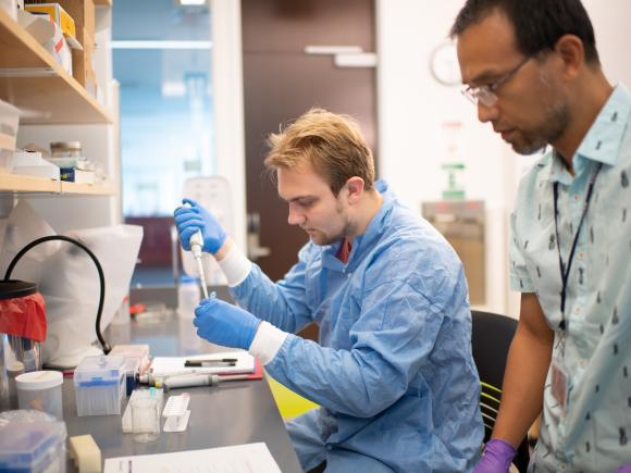 Student in lab coat and gloves preparing samples for DNA extraction