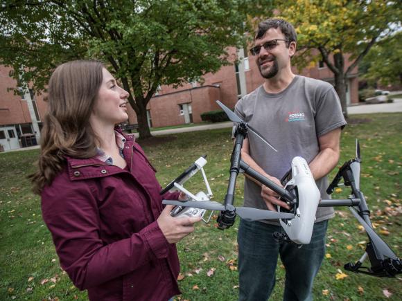 Student holding a controller as she talks to her professor who is holding a quadcopter drone.