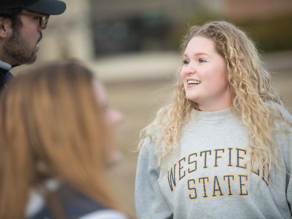 Smiling female with long hair and a Westfield State sweatshirt with friends out on the campus green