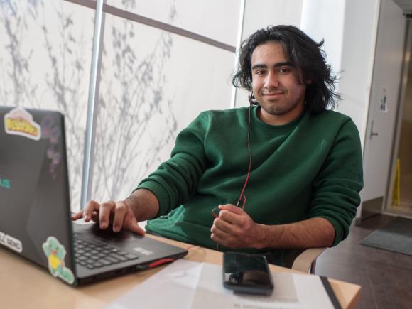 Male student smiling at camera as he works on laptop