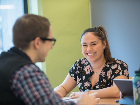 Smiling female student talks to friend across the table from her