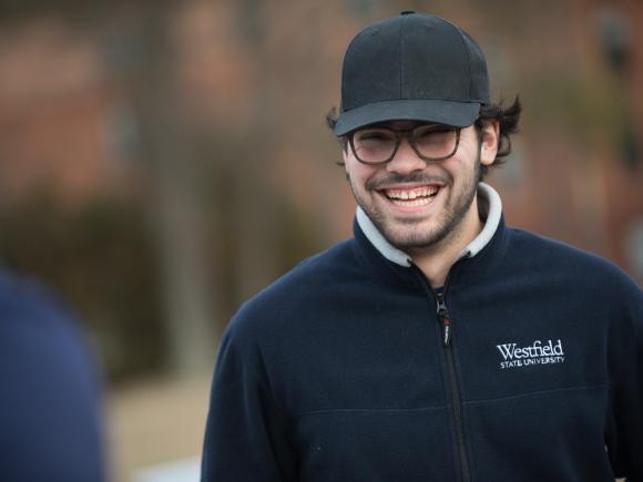 Smiling male student in glasses and ball cap on the campus green