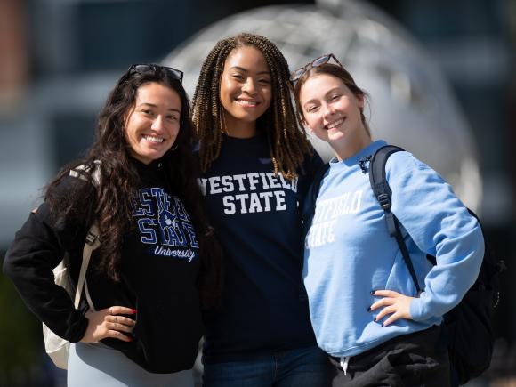 Image of three female students smiling at the camera in front of the Globe on the campus green