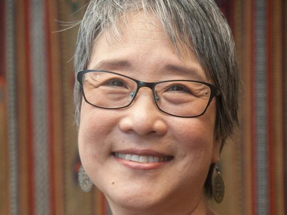 An Asian woman is smiling in front of a patterned wall decor