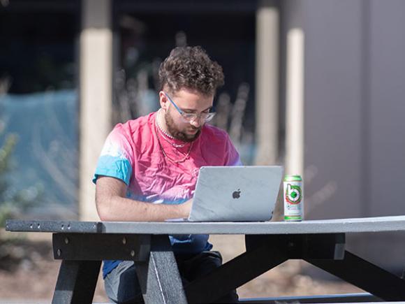 male student outside at picnic table working