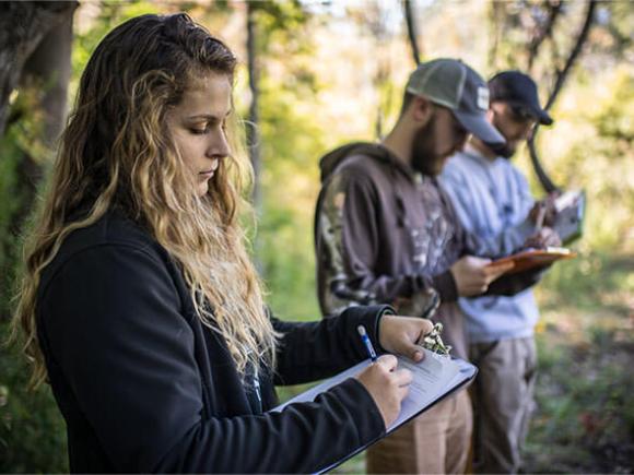Three students making notes while standing outside in a nature area.