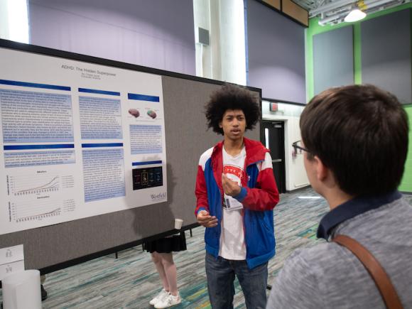 A male student displays a presentation of a poster to another student.