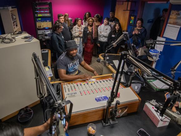 A group of students and an instructor gather around a recording studio.